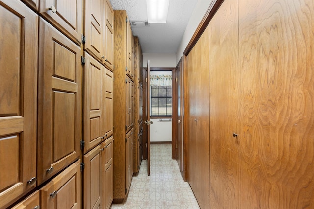 hallway with visible vents, a textured ceiling, and light floors