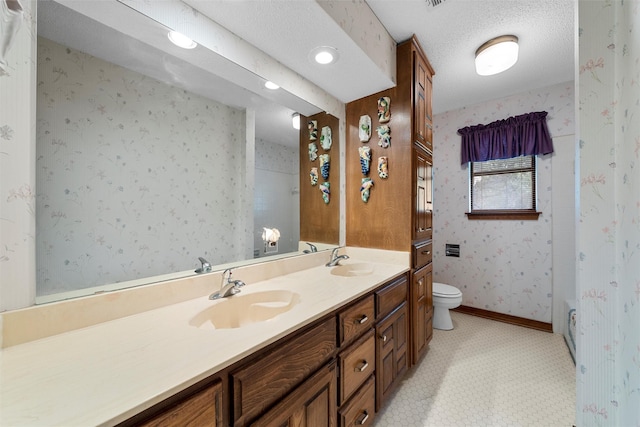 bathroom featuring toilet, double vanity, wallpapered walls, and a sink