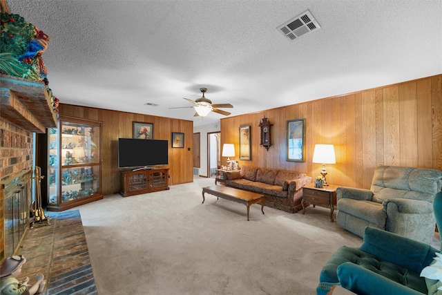 living room featuring ceiling fan, a brick fireplace, wood walls, carpet, and visible vents