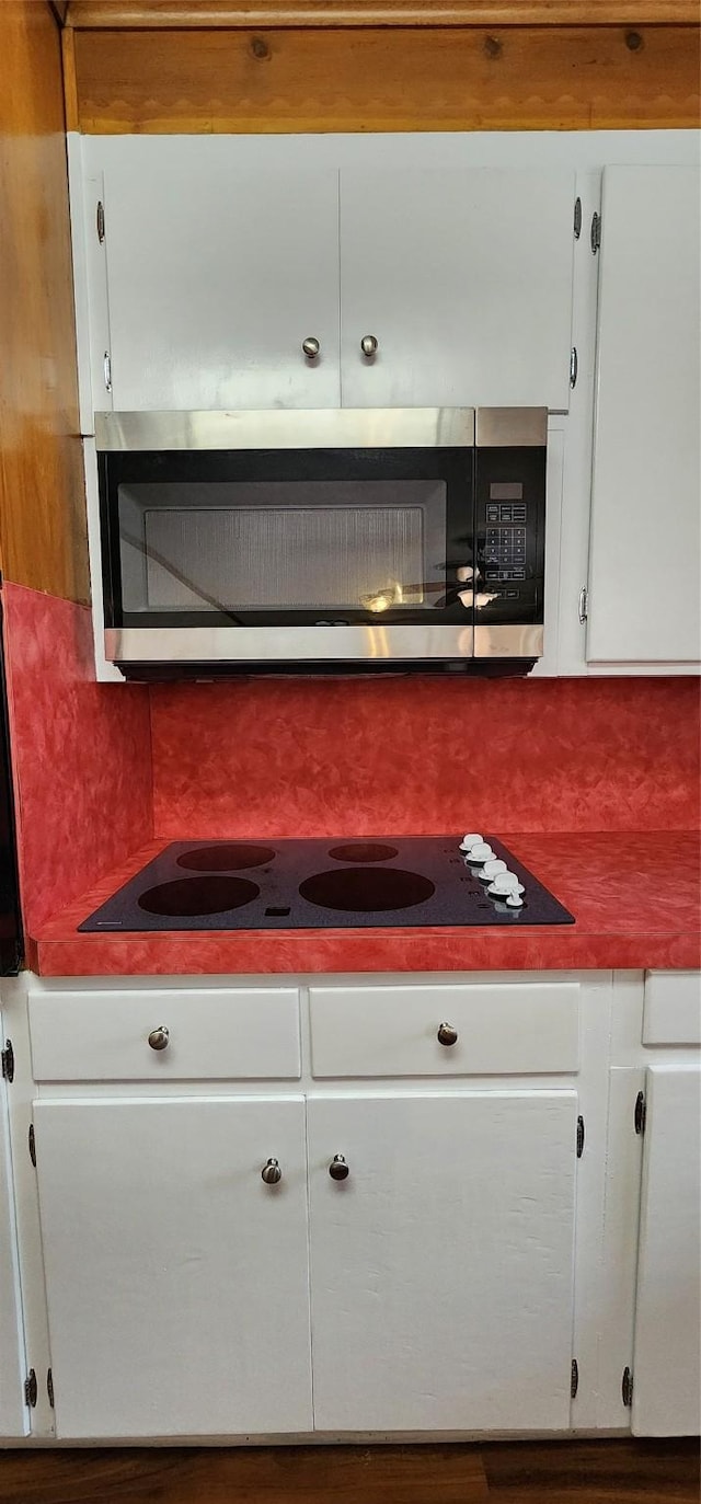 interior details featuring white cabinets, stainless steel microwave, and tasteful backsplash