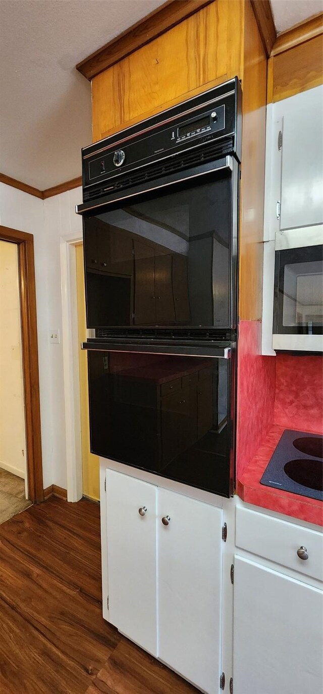 interior details featuring ornamental molding, dark wood-style flooring, black appliances, and white cabinets
