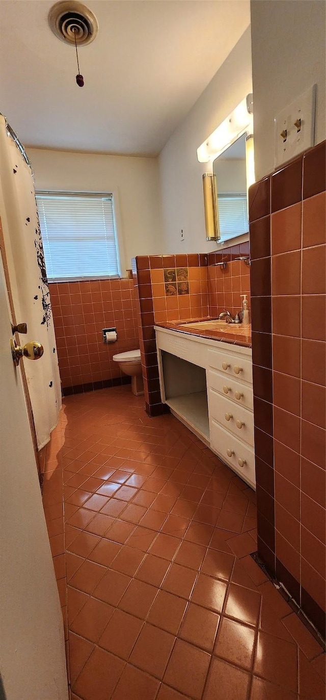 bathroom featuring tile patterned flooring, vanity, toilet, tile walls, and visible vents