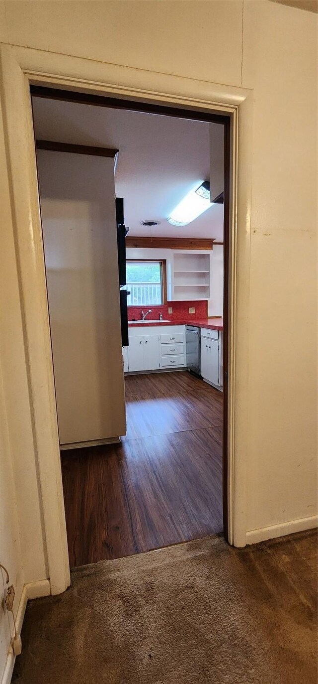 hall featuring baseboards, dark wood-style floors, a sink, and dark colored carpet