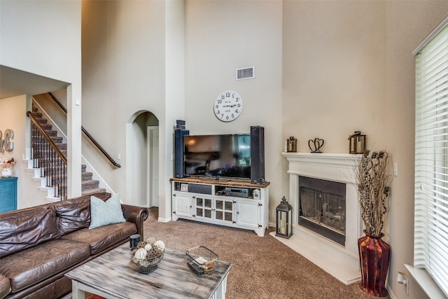 1821 Beacon Beach Way, Wylie, TX 75098 - living room with carpet flooring, a high ceiling, a glass covered fireplace, stairs, and arched walkways