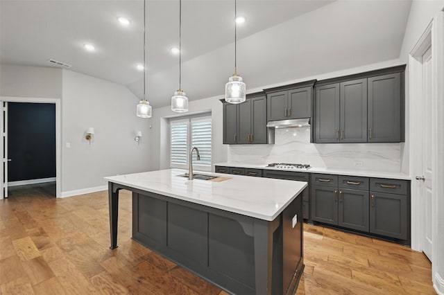 kitchen featuring light stone counters, a sink, stainless steel gas cooktop, lofted ceiling, and under cabinet range hood