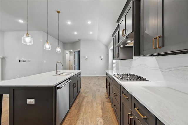 kitchen with appliances with stainless steel finishes, a center island with sink, a sink, light stone counters, and light wood-style floors