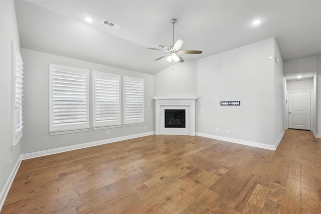 unfurnished living room with a ceiling fan, visible vents, vaulted ceiling, a glass covered fireplace, and light wood-style floors