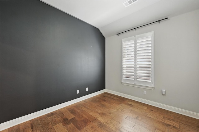 unfurnished room featuring visible vents, baseboards, wood finished floors, and vaulted ceiling