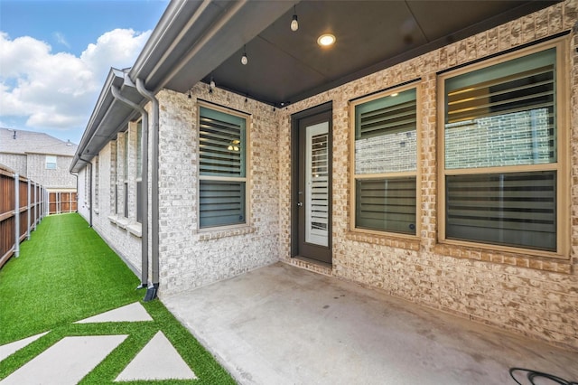 entrance to property featuring fence, a lawn, and a patio area