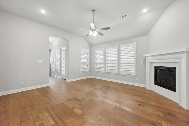 unfurnished living room with a ceiling fan, arched walkways, wood finished floors, and vaulted ceiling