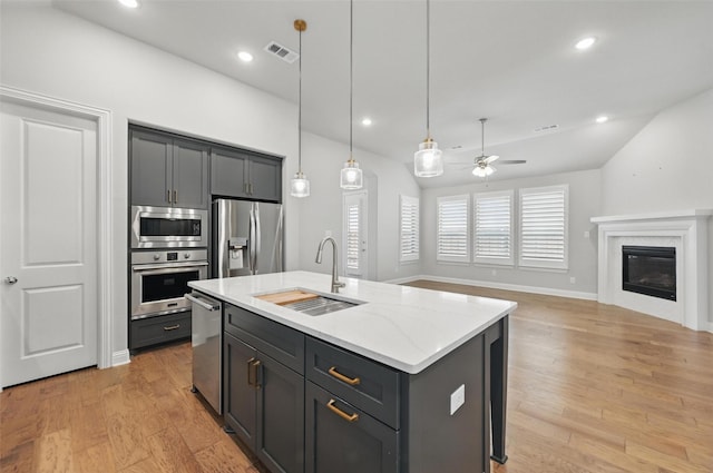 kitchen with a ceiling fan, appliances with stainless steel finishes, light stone countertops, a sink, and light wood-style floors