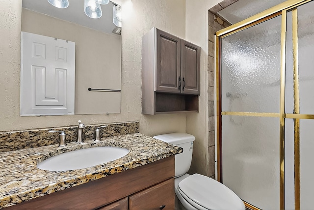 full bath with vanity, a textured wall, a shower stall, and toilet