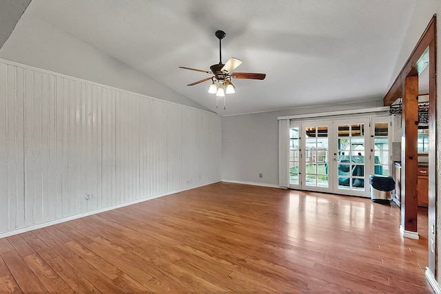 unfurnished room with a ceiling fan, light wood-style flooring, vaulted ceiling, and wooden walls