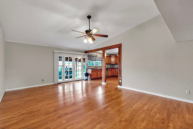 unfurnished room featuring baseboards, ceiling fan, a sink, light wood-style flooring, and vaulted ceiling