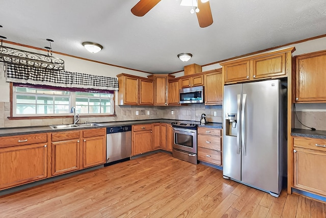kitchen featuring brown cabinets, dark countertops, appliances with stainless steel finishes, a sink, and a ceiling fan