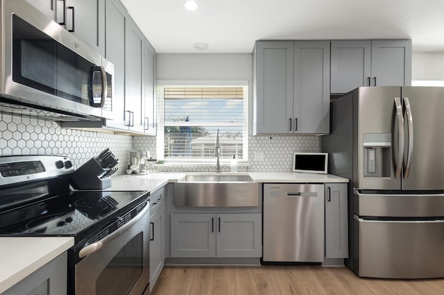 kitchen featuring appliances with stainless steel finishes, gray cabinetry, a sink, light wood-style floors, and light countertops