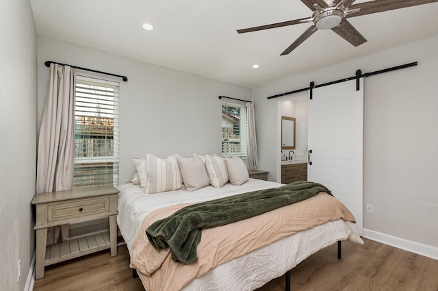 bedroom with a barn door, wood finished floors, a sink, baseboards, and recessed lighting