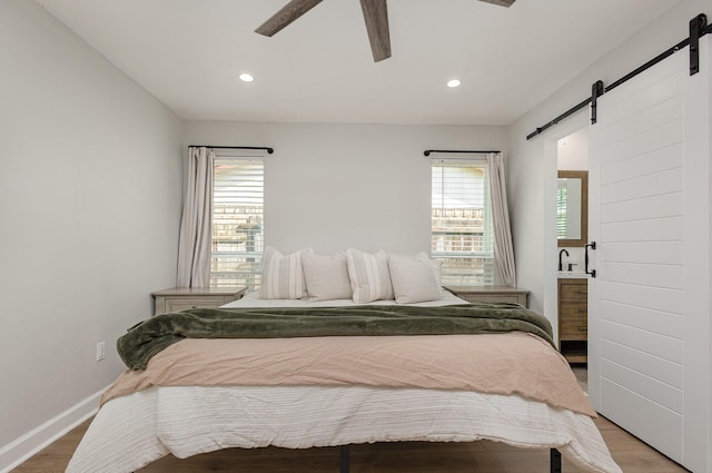 bedroom featuring a barn door, light wood-style flooring, recessed lighting, baseboards, and ceiling fan
