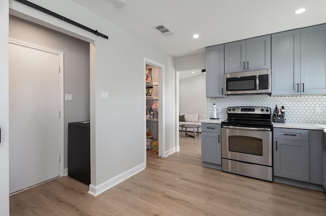 kitchen with stainless steel appliances, gray cabinetry, light countertops, tasteful backsplash, and light wood-style flooring