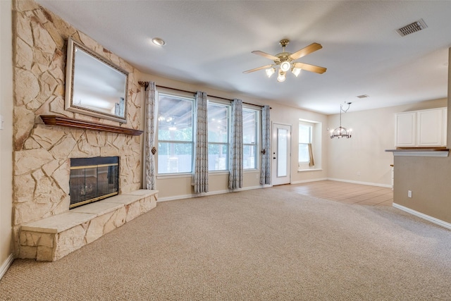 unfurnished living room featuring a stone fireplace, visible vents, baseboards, ceiling fan with notable chandelier, and light carpet