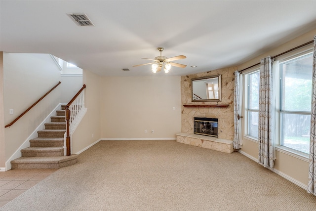 unfurnished living room with baseboards, a ceiling fan, a stone fireplace, and visible vents
