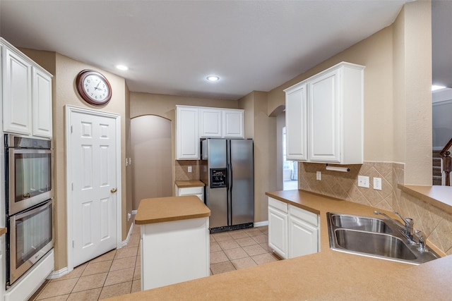 kitchen featuring appliances with stainless steel finishes, a sink, arched walkways, white cabinetry, and light tile patterned floors