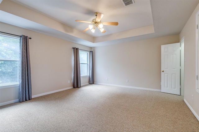 carpeted spare room featuring plenty of natural light, ceiling fan, a tray ceiling, and visible vents
