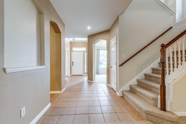 entrance foyer with light tile patterned flooring, a textured wall, arched walkways, baseboards, and stairway