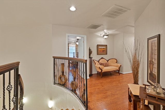 corridor with baseboards, visible vents, wood finished floors, and an upstairs landing