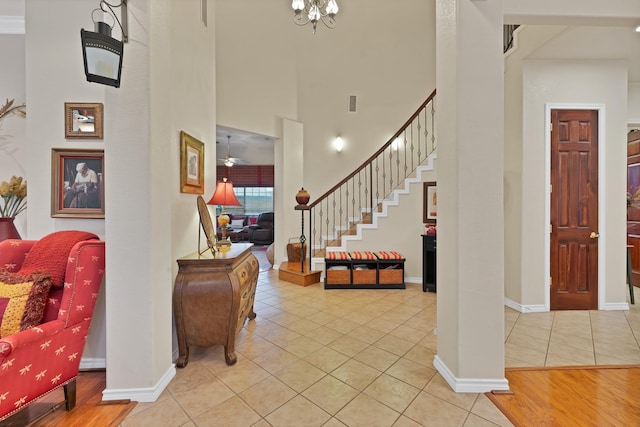foyer entrance with stairs, light tile patterned flooring, baseboards, a high ceiling, and a notable chandelier