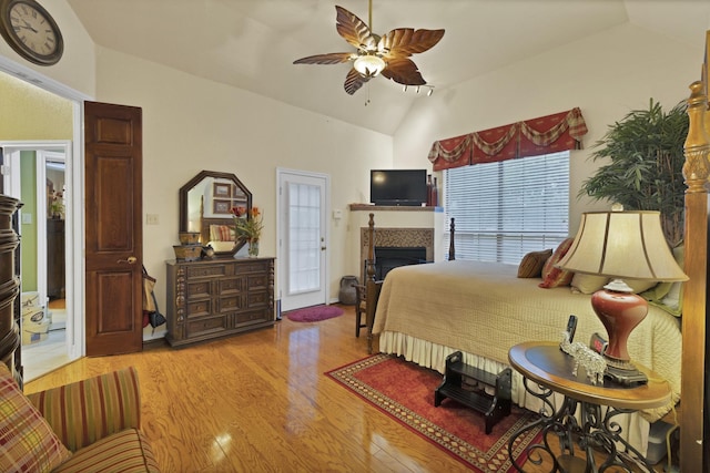 bedroom featuring lofted ceiling, access to exterior, ceiling fan, light wood-type flooring, and a tile fireplace