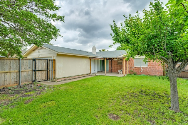 back of house with a chimney, a gate, a patio area, a fenced backyard, and a yard