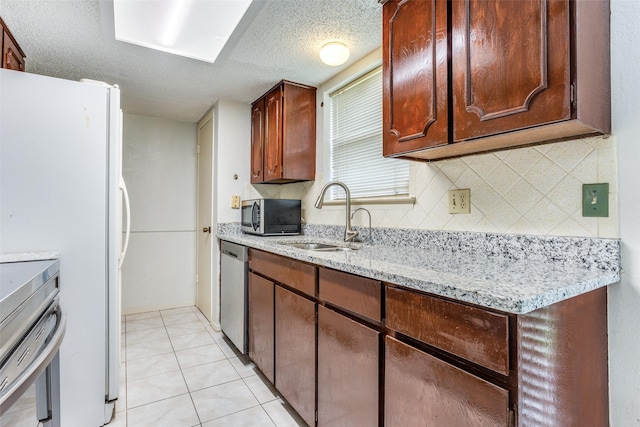 kitchen with light stone countertops, appliances with stainless steel finishes, a sink, a textured ceiling, and decorative backsplash