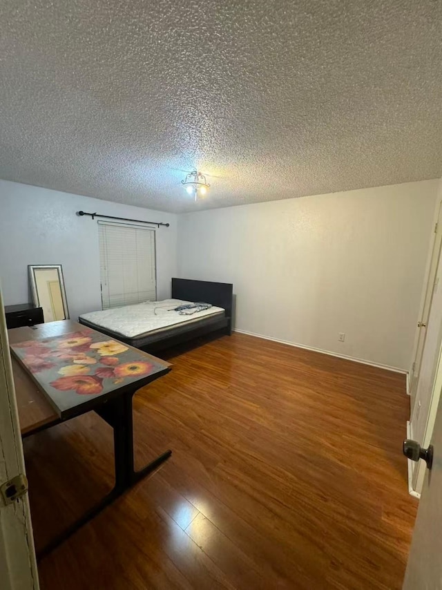 bedroom with baseboards, a textured ceiling, and wood finished floors