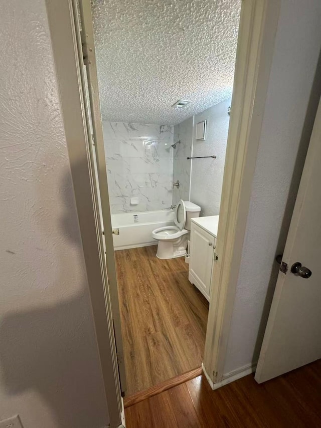 bathroom with a textured ceiling, toilet, wood finished floors, and  shower combination