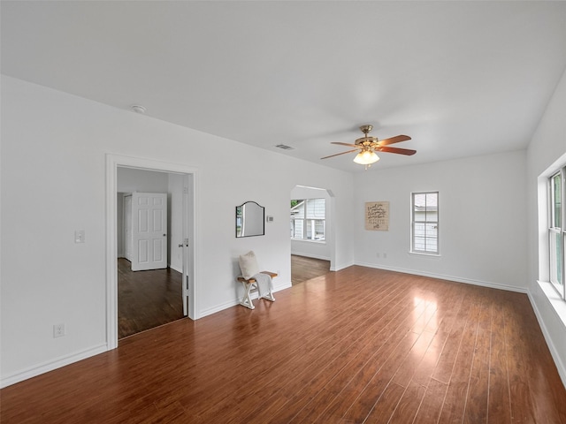 unfurnished living room with arched walkways, dark wood finished floors, a ceiling fan, baseboards, and visible vents
