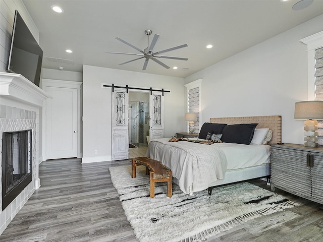 1018 Chaparrel Ln, Graford, TX 76449 - bedroom featuring a barn door, wood finished floors, recessed lighting, a tiled fireplace, and baseboards