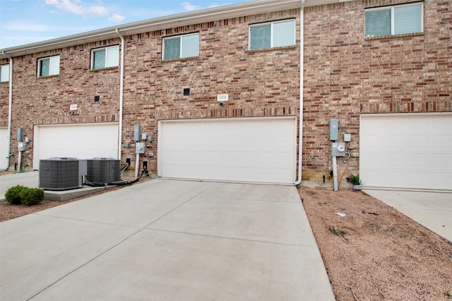 exterior space featuring central AC unit, an attached garage, concrete driveway, and brick siding