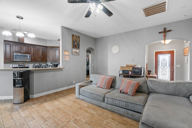 living area featuring a ceiling fan, visible vents, arched walkways, baseboards, and light wood finished floors