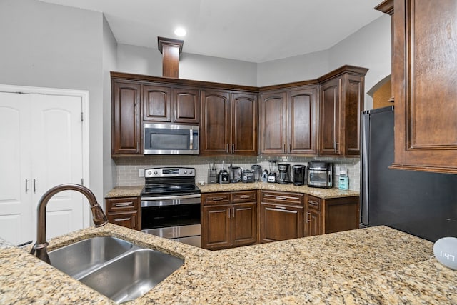 kitchen featuring dark brown cabinetry, light stone countertops, tasteful backsplash, a sink, and stainless steel appliances