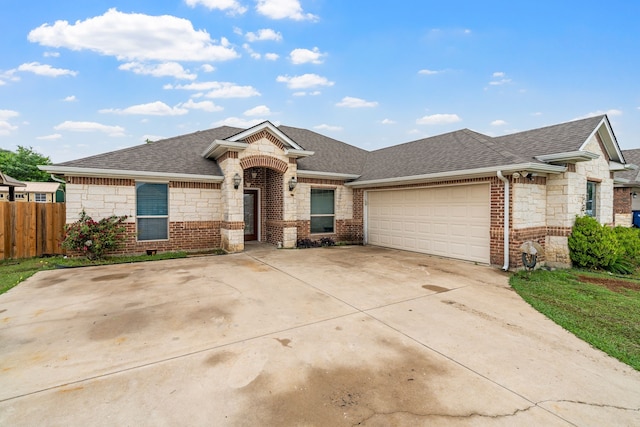 ranch-style home featuring fence, roof with shingles, brick siding, an attached garage, and driveway