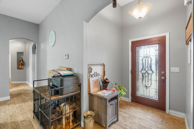 foyer featuring light wood-style floors, arched walkways, and baseboards