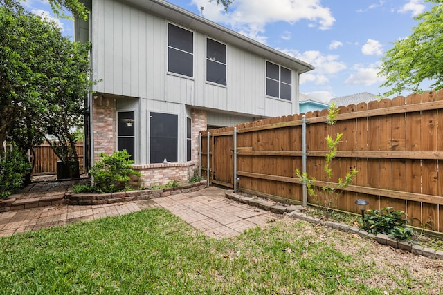rear view of house with brick siding, a fenced backyard, a yard, and a patio
