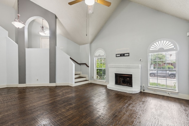 unfurnished living room featuring a ceiling fan, a fireplace, wood finished floors, stairway, and high vaulted ceiling