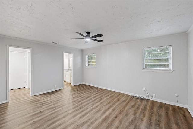spare room with visible vents, ornamental molding, wood finished floors, baseboards, and a ceiling fan