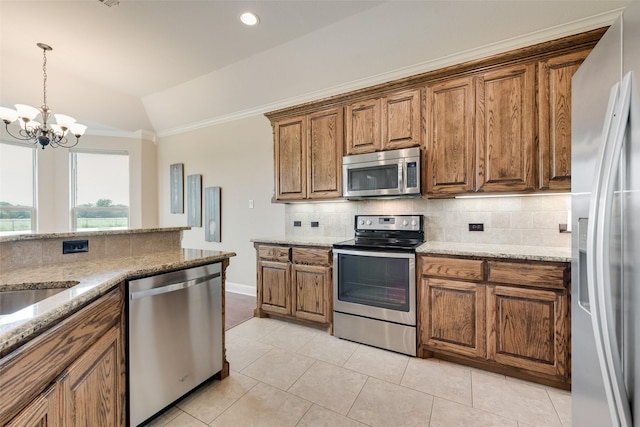 kitchen featuring backsplash, appliances with stainless steel finishes, vaulted ceiling, brown cabinets, and a chandelier