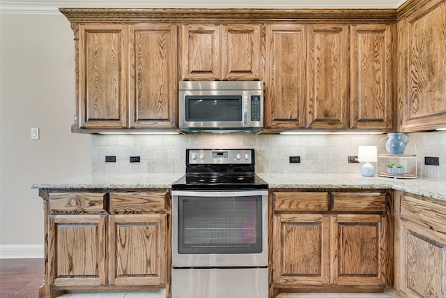 kitchen with brown cabinetry, baseboards, tasteful backsplash, light stone counters, and stainless steel appliances