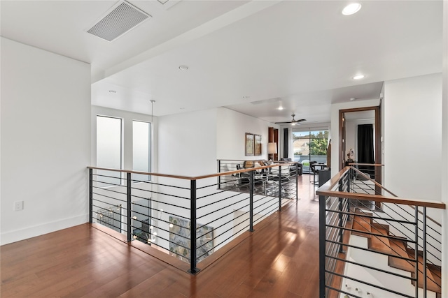 hallway featuring visible vents, wood finished floors, baseboards, recessed lighting, and an upstairs landing