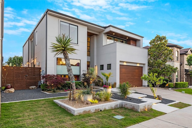 contemporary house with fence, a balcony, concrete driveway, an attached garage, and stucco siding