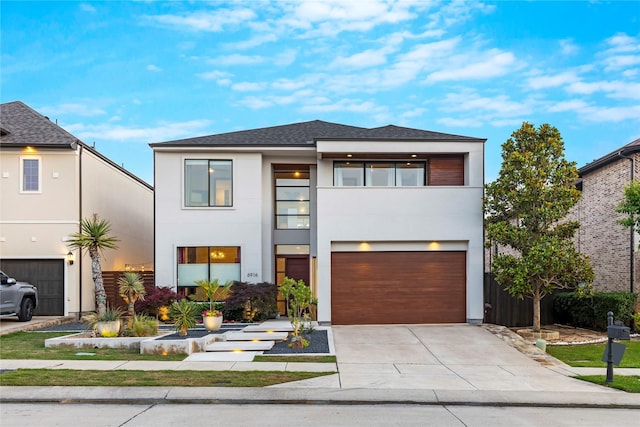 contemporary house with roof with shingles, an attached garage, stucco siding, concrete driveway, and a balcony